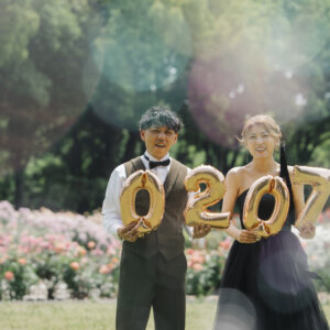 薔薇の咲く庭園で『0207』のバルーンを持つオリーブのベストの新郎と黒いドレスの花嫁。バルーンを使った洋装前撮りのアイテムカット