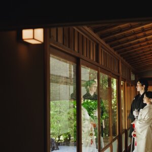 木造の渡り廊下で向かい合う黒紋付袴の新郎と白無垢の花嫁を引きでとらえた一枚。日本庭園の渡り廊下で撮る和装前撮り