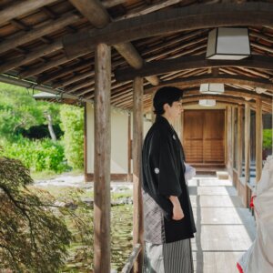 蓮池を望む木造の渡り廊下で離れて立つ黒紋付袴の新郎と白無垢の花嫁。白鳥庭園で撮る和装ロケーションフォト