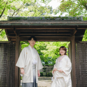 瓦屋根の木の門の下に立つ白い羽織袴の新郎と白い色打掛の花嫁。岡崎公園で撮る和装ロケーションフォト