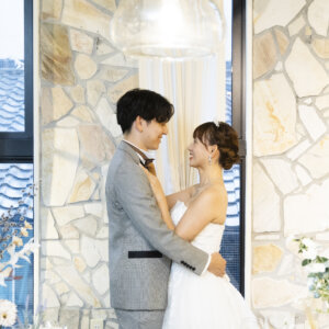 ドライフラワーのテーブル越しに、石張りの壁の前で抱き合って見つめ合う新郎新婦。カフェ風の名古屋のスタジオフォト