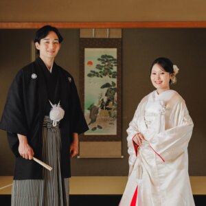 白鳥庭園にて、松の絵の掛け軸の前に並んで立つ黒紋付袴の新郎と白無垢の花嫁。日本家屋の和室で撮る和装前撮りの正面カット