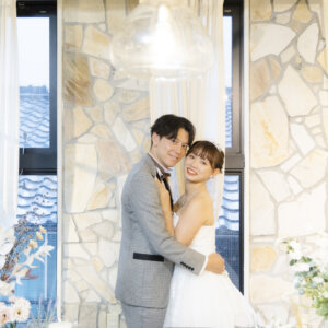 石張りの壁とペンダントライトのスタジオで抱き合って笑う、グレーのタキシードの新郎とウェディングドレスの花嫁の前撮り