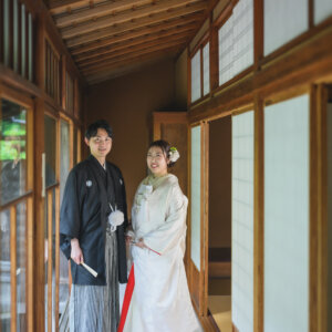障子の続く廊下に立つ黒紋付袴の新郎と白無垢の花嫁を縦位置でとらえた一枚。日本家屋で撮る和装前撮り