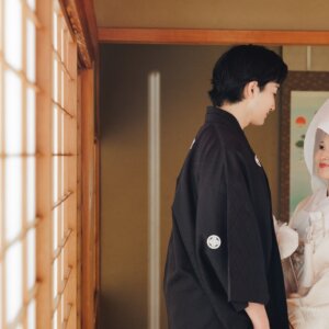 障子の前で向かい合う黒紋付袴の新郎と綿帽子の白無垢の花嫁。日本家屋で撮る和装前撮り