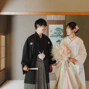 掛け軸の前でピンクのブーケを持って笑い合う白い色打掛の花嫁と黒紋付袴の新郎。白鳥庭園の和室で撮る和装前撮り