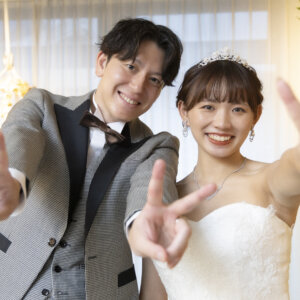 カメラに向かって両手でピースをする、グレーのタキシードの新郎とティアラのウェディングドレスの花嫁。遊び心のある名古屋のスタジオフォト