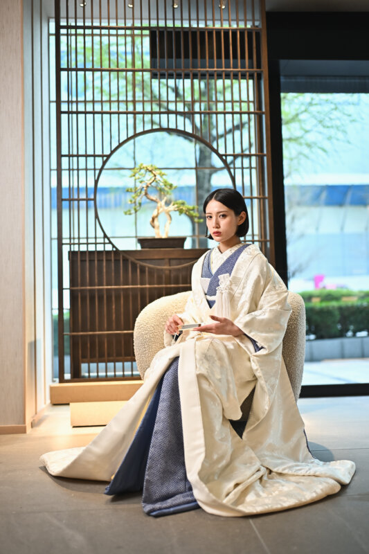 丸窓と格子を背に椅子に座る紺の襟元の白い色打掛の花嫁。名古屋のスタジオで撮る和装前撮りの衣装写真