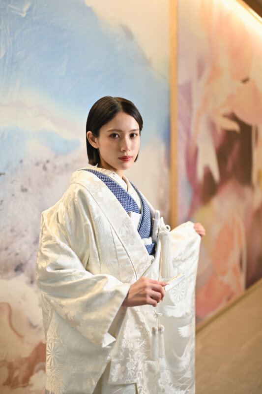紺の襟元の白い色打掛の袖を持ち、アートの壁の前に立つ花嫁。名古屋のスタジオで撮る和装前撮りで選べる白い色打掛の衣装写真
