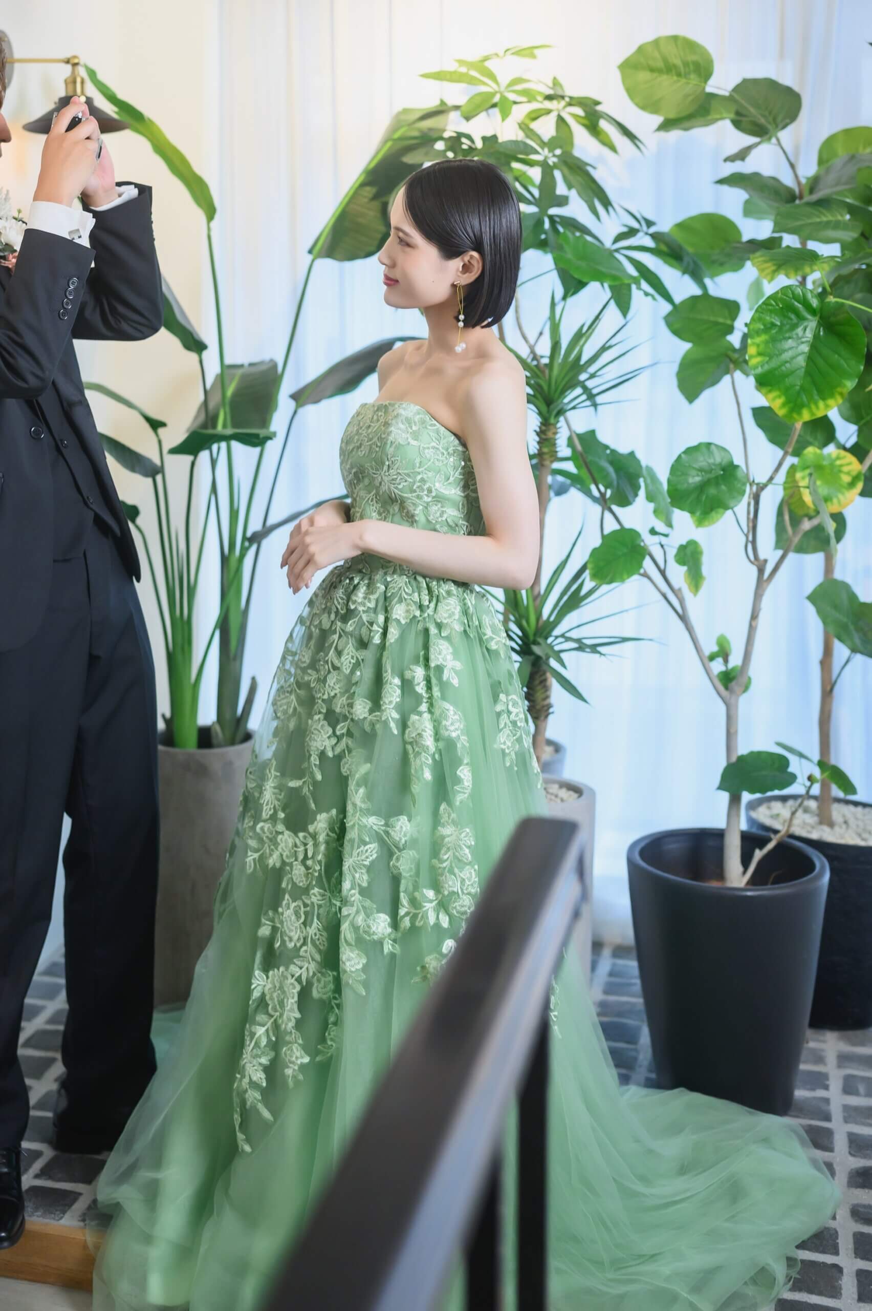 大きな観葉植物を背に、長い裾を広げて佇むグリーンのカラードレス姿の花嫁。名古屋のスタジオで叶えるウェディングフォト