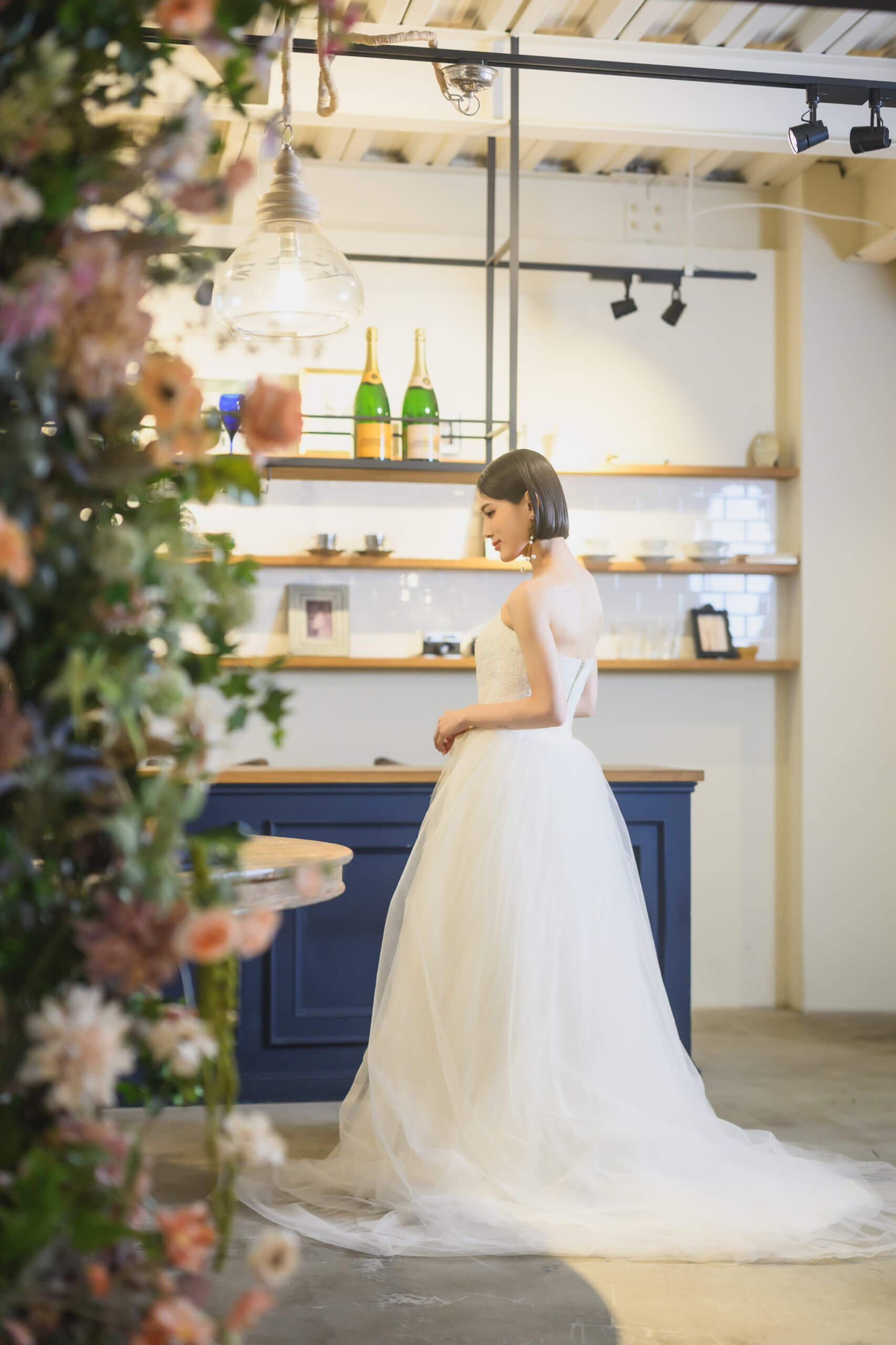 ネイビーのカウンターを背に佇む、白いチュールのウェディングドレス姿の花嫁の後ろ姿。カフェ風スタジオでの前撮りポートレート