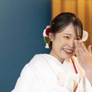 ファーストミートで涙をぬぐいながら笑う、白無垢に赤い髪飾りを合わせた花嫁。感動の瞬間を残す和装前撮りのカット
