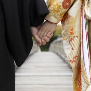 木の橋の上で手をつなぐ、黒紋付の新郎と金地に菊の柄の色打掛の花嫁の手元。結婚指輪が光る和装前撮りの手つなぎカット