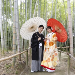 青竹の林を背に、白と赤の和傘をさして寄り添う紋付袴の新郎と色打掛の花嫁。白鳥庭園の竹林で撮る和装ロケーションフォト