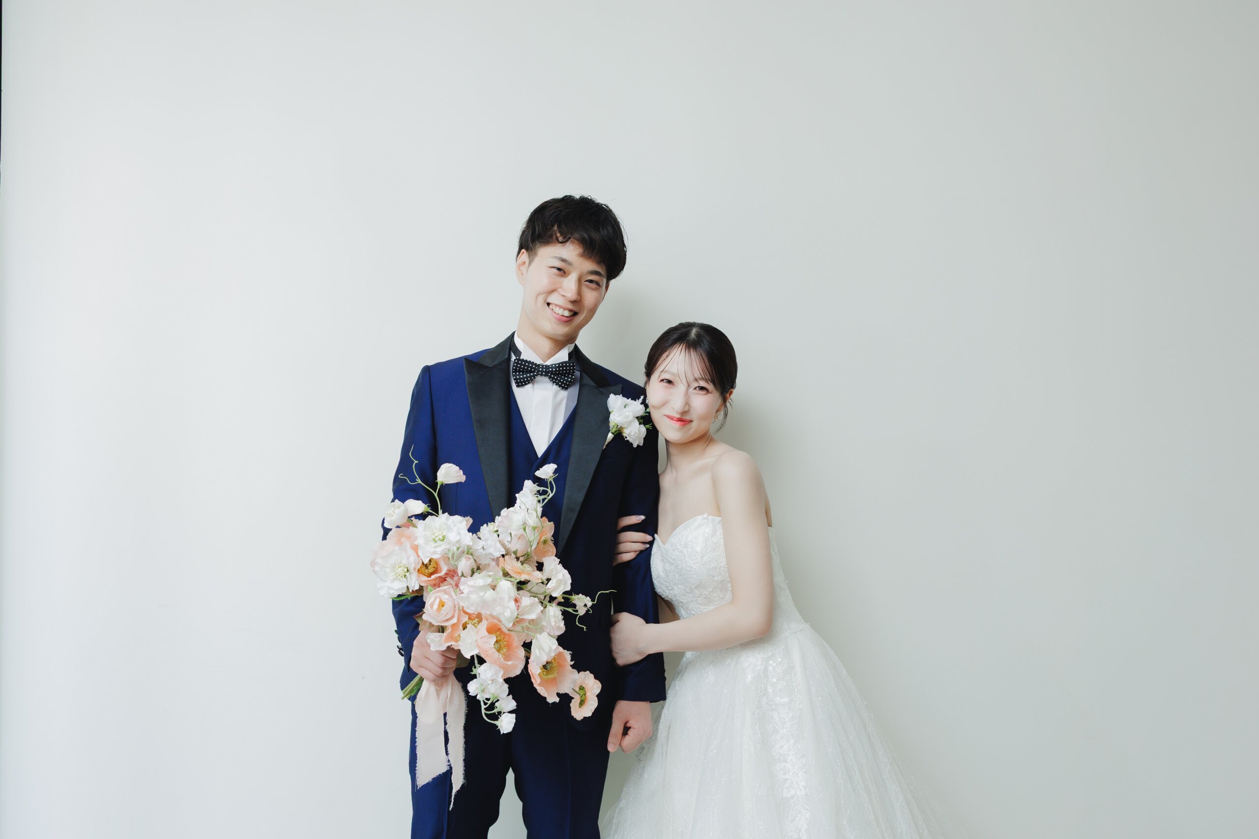 木漏れ日の中、ベージュのタキシード姿の新郎に寄り添い、ピンクのブーケを持つ新婦