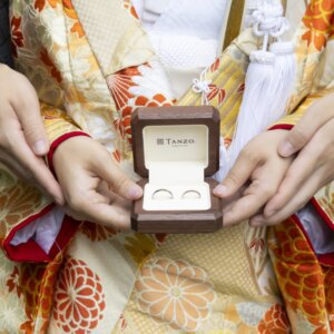 菊柄の色打掛の袖の前で、結婚指輪の入ったリングボックスを二人で持つ新郎新婦の手元。和装前撮りで撮りたい指輪のカット