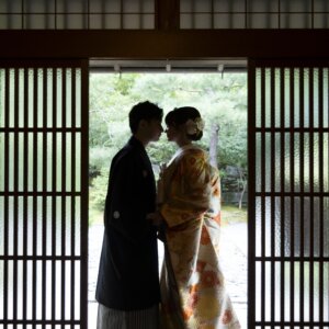 格子戸の間から庭の光を背に、おでこを寄せ合う紋付袴の新郎と色打掛の花嫁のシルエット。茶室で撮る和装前撮りのおでこ合わせ