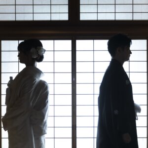 障子の明かりの中で向かい合う紋付袴の新郎と白無垢の花嫁のシルエット。和室で撮る和装前撮りのシルエットショット