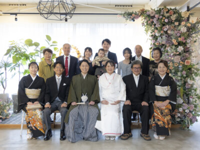 フラワーウォールのあるスタジオで、白無垢の花嫁と羽織袴の新郎を囲むご家族とご親族の集合写真。名古屋のスタジオで撮る家族写真のフォトウェディング